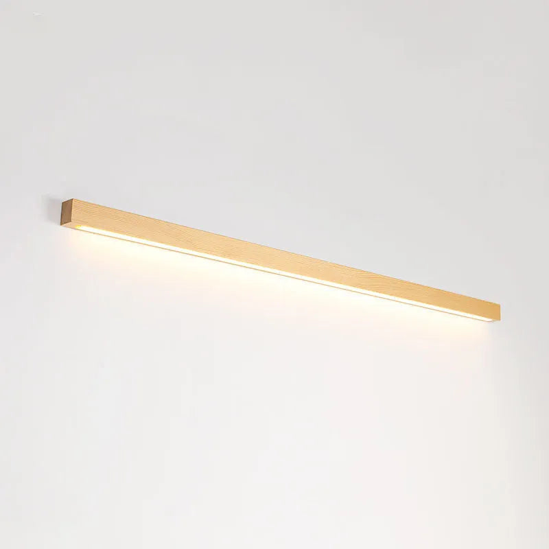 Long, slim walnut-coloured wooden wall lamp with integrated LED lighting on a plain wall.