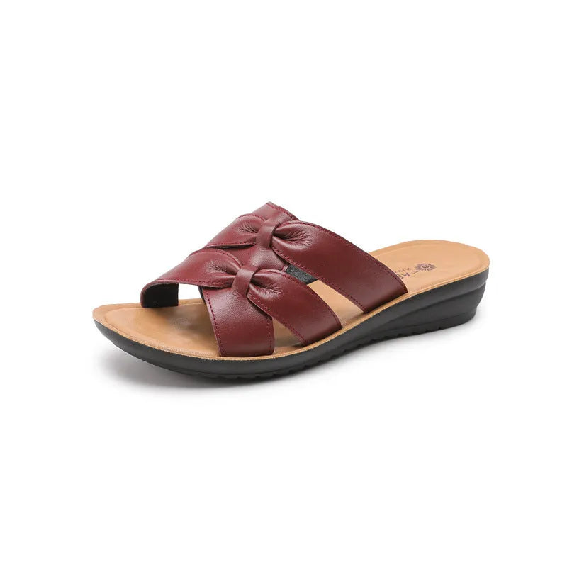 Beige cowhide leather women's slippers with a non-slip sole on a wooden floor.