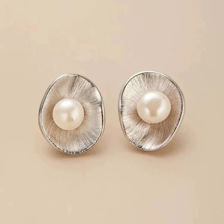 Gold tone geometric stud earrings with a central freshwater pearl on a silver needle post.