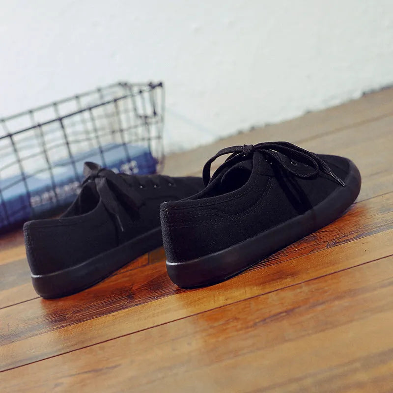 All-black women's canvas flat shoes with lace-up front and rubber soles.