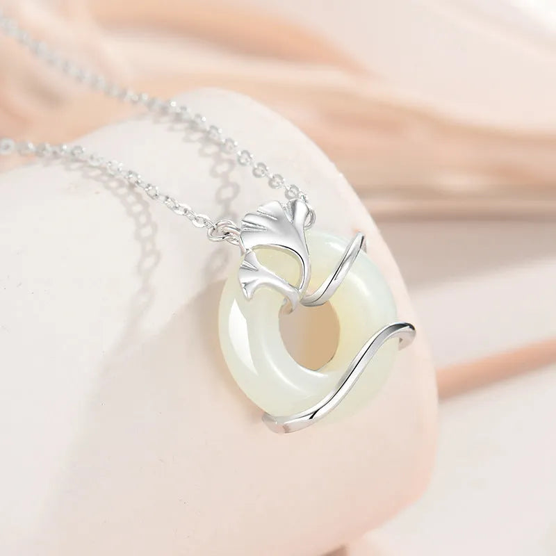 Close-up of a sterling silver peace buckle necklace with a cross chain and ginkgo details, shown in a gold tone.