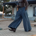 Grey men's high-waisted pleated trousers with a wide-leg fit on a hanger.