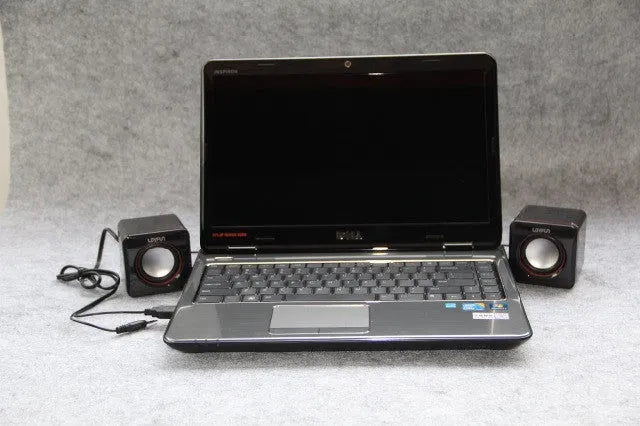 Black small square USB-powered computer speaker on desktop next to monitor