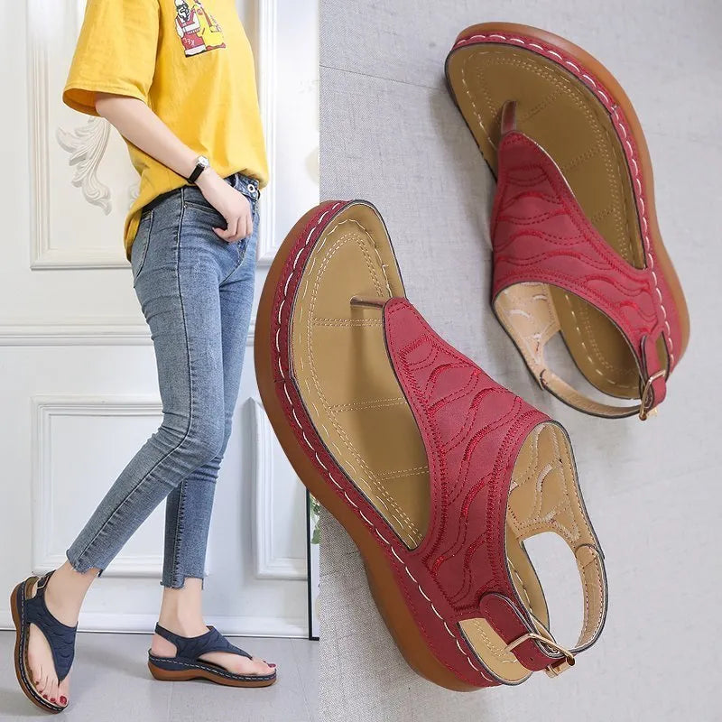 Women's beige wedge heel flip flop sandals with an adjustable buckle strap on a wooden deck.