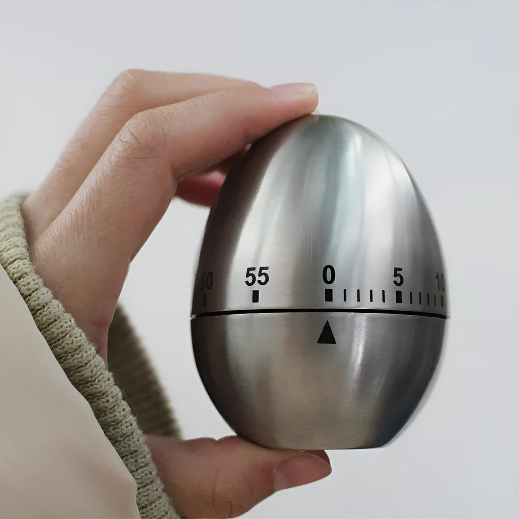 Stainless steel egg-shaped mechanical kitchen timer on a kitchen counter
