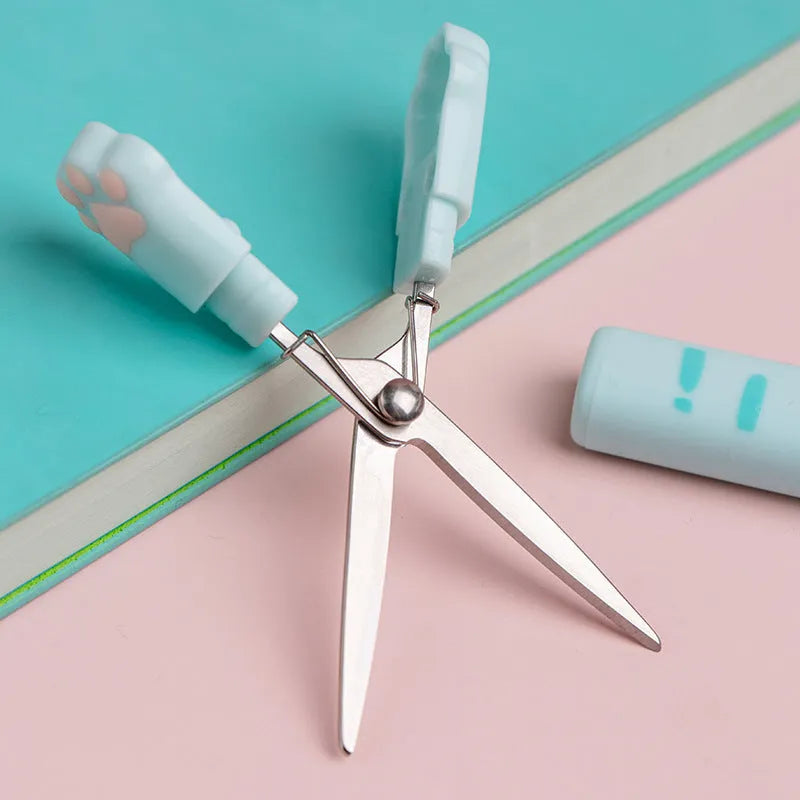 Portable folding cat paw scissors in blue, showing compact size next to a pencil for scale.