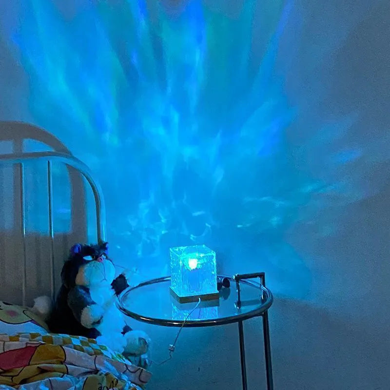 Square crystal LED table lamp projecting blue water ripple light patterns on a wall.