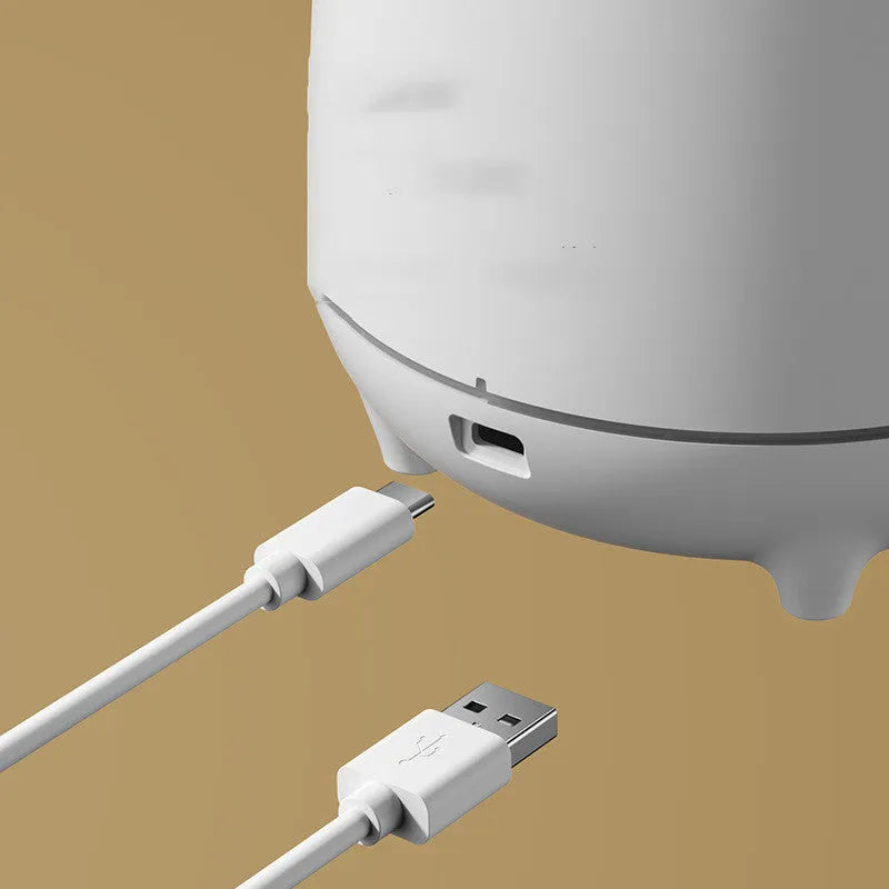 White volcano-shaped ultrasonic humidifier with USB cable on table emitting mist