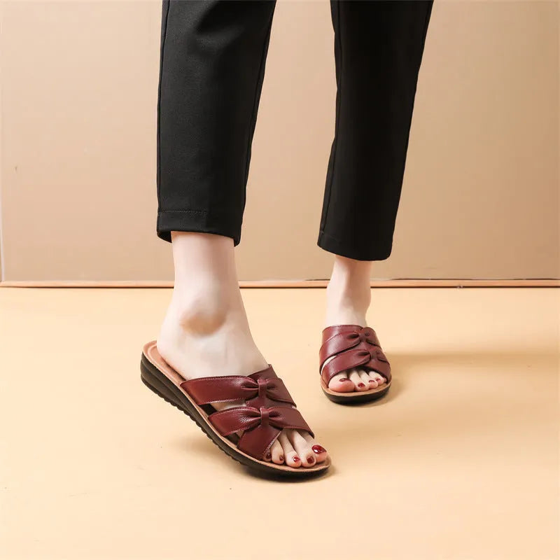 Beige cowhide leather women's slippers with a non-slip sole on a wooden floor.