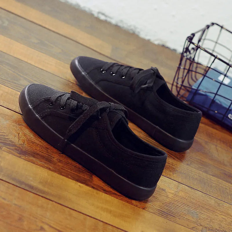 All-black women's canvas flat shoes with lace-up front and rubber soles.