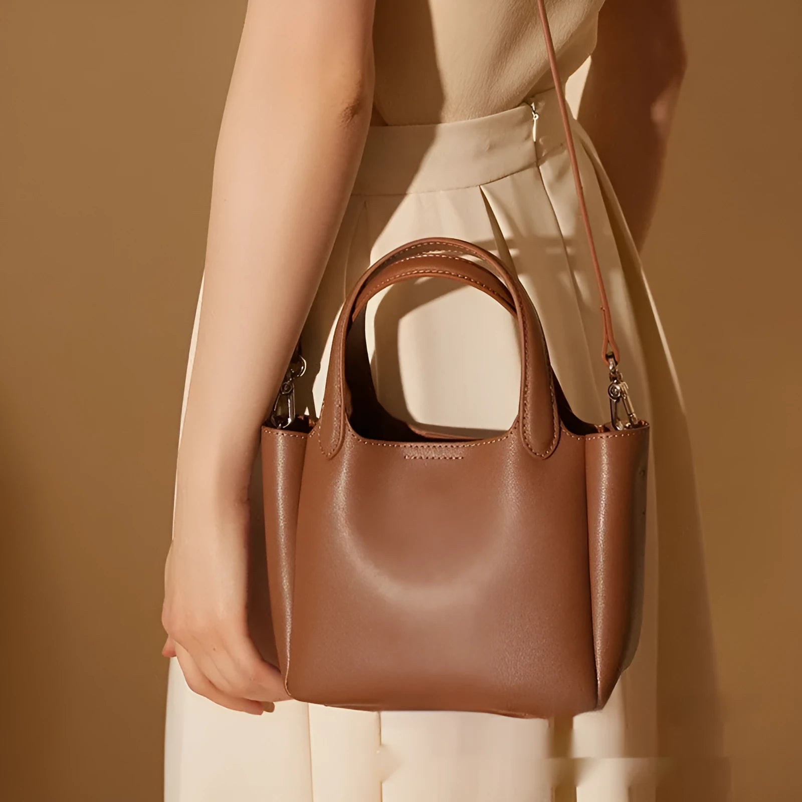 Brown cattlehide leather cross body bucket bag with square vertical shape and visible stitching