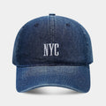 Light blue denim peaked cap with embroidered letters on a dome crown, showing adjustable strap.