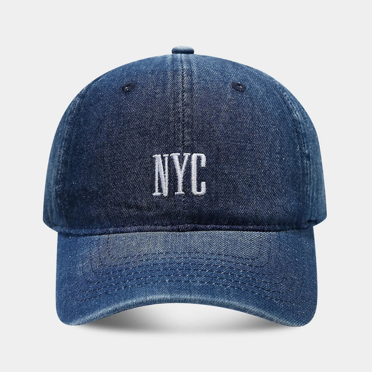 Light blue denim peaked cap with embroidered letters on a dome crown, showing adjustable strap.