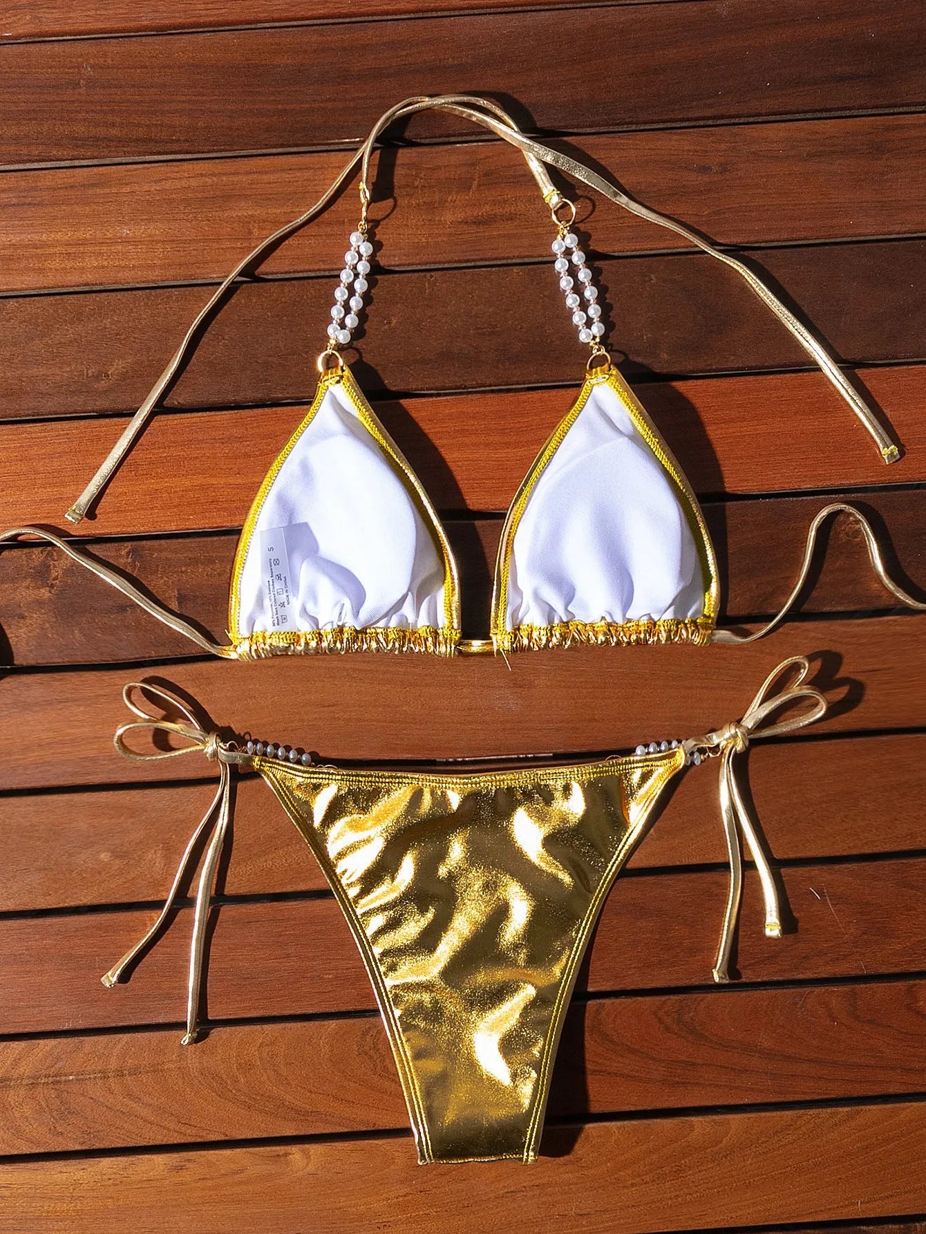 Gold halter neck bikini top with lace-up front and pearl chain, paired with brief-style bottoms