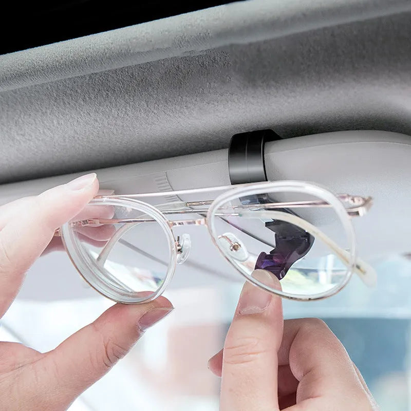 Black plastic clip for car sunshade holding sunglasses and a ticket.