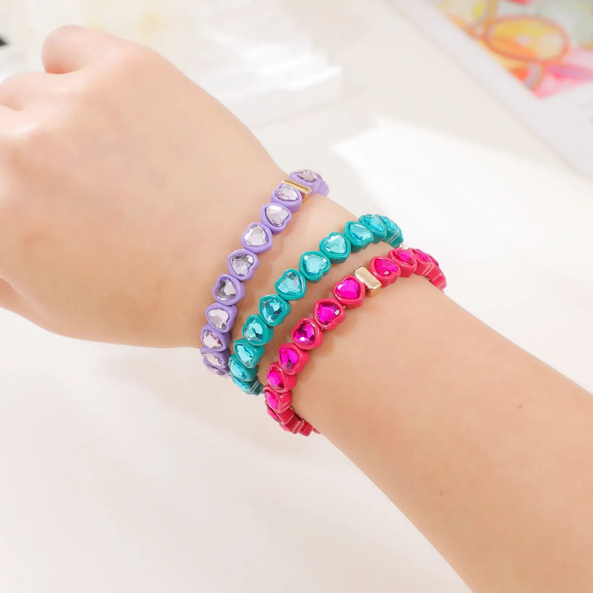 Rainbow enamel heart pendant on a stretch alloy bracelet, shown in multiple colour options.