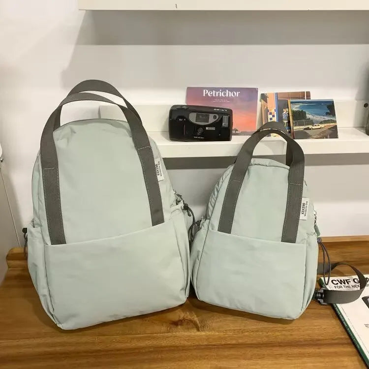 Solid colour nylon backpack in multiple colours with curved shoulder straps, shown in small and large sizes.