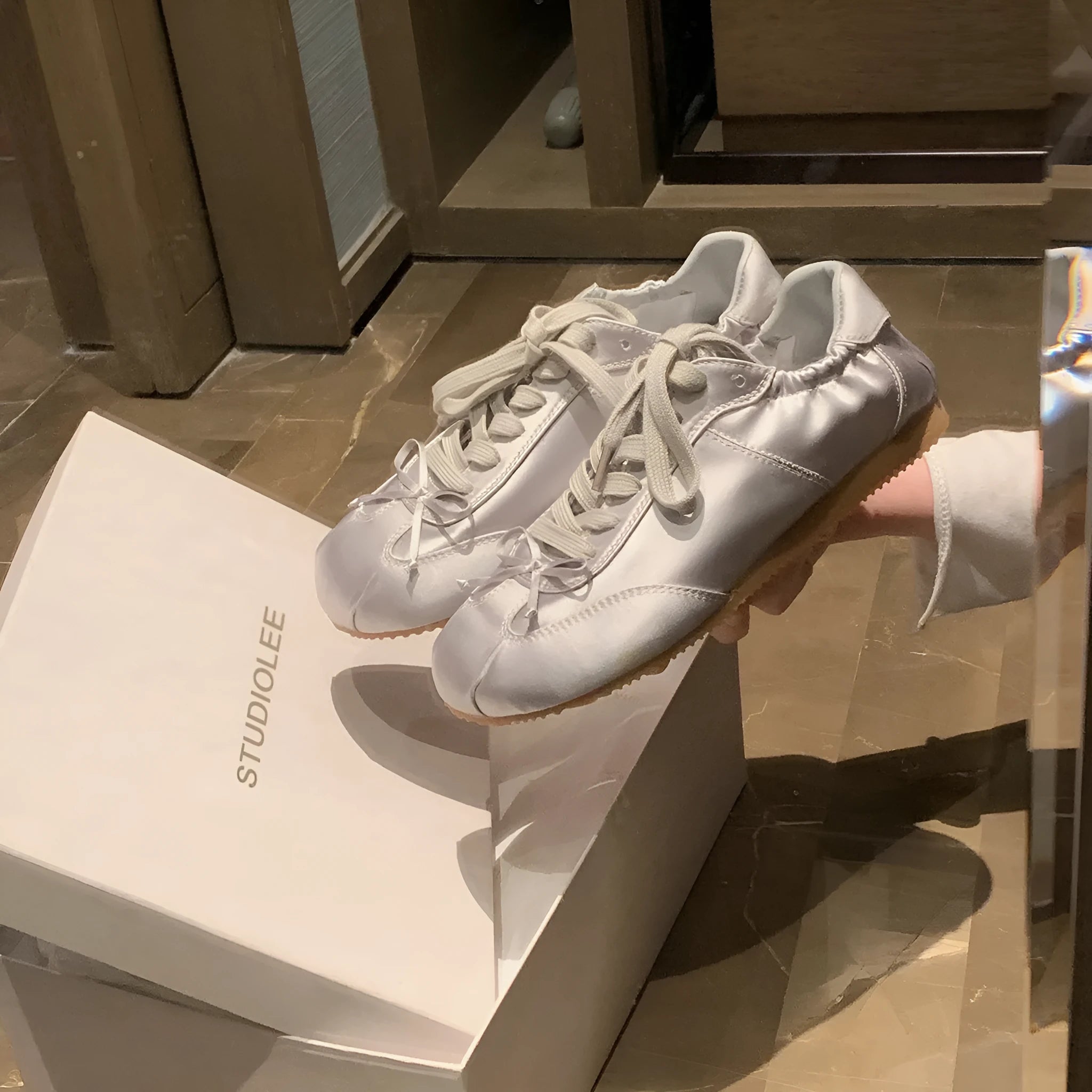 Women's silver satin ballet flats with round toe and white front lace-up on a rubber sole.