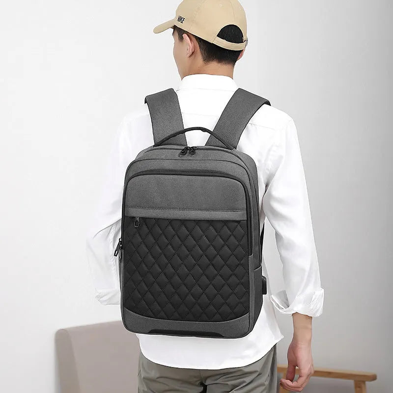 Men's solid colour Oxford cloth travel backpack with curved shoulder strap shown in black, blue, and grey.