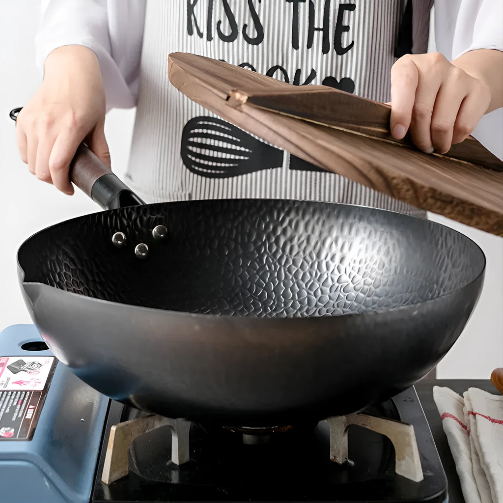 Black traditional iron wok with wooden handle, shown with glass lid.
