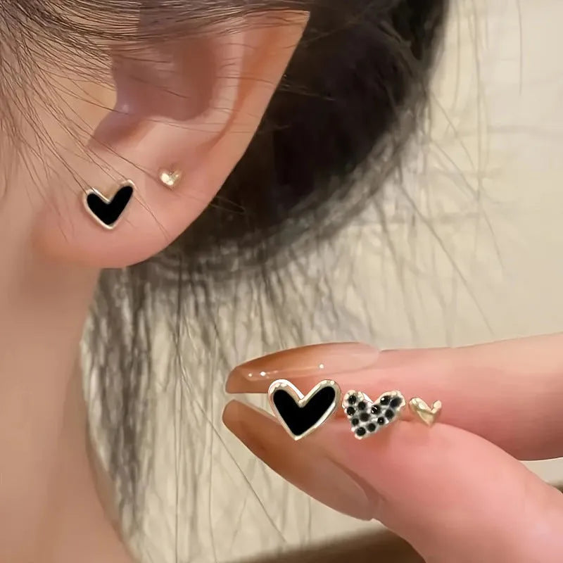 Set of three pairs of women's heart-shaped alloy earrings in gold, black, black and white, and pink colours.
