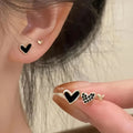 Set of three pairs of women's heart-shaped alloy earrings in gold, black, black and white, and pink colours.