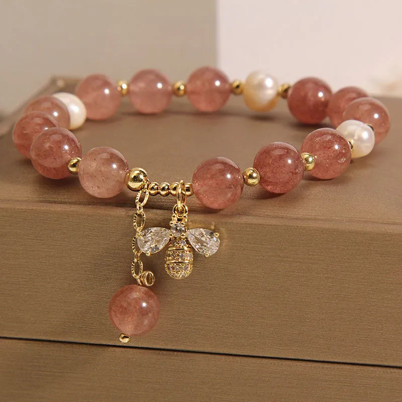 Close-up of a women's bracelet with strawberry quartz, freshwater pearls, a bee charm, and zircon accents on an alloy chain.