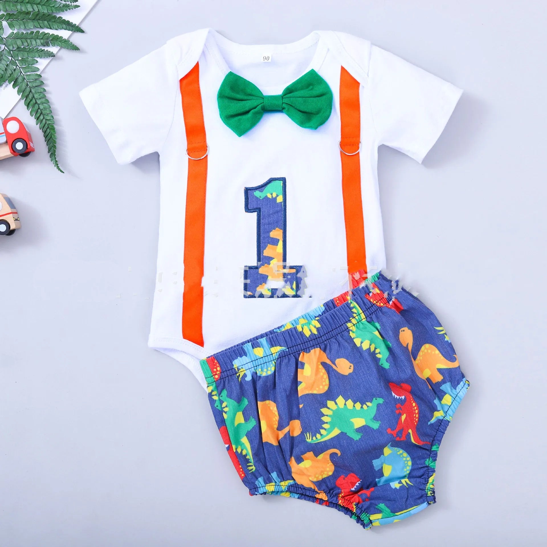 Baby wearing a blue cotton romper with shorts, a bow, and dinosaur print details.