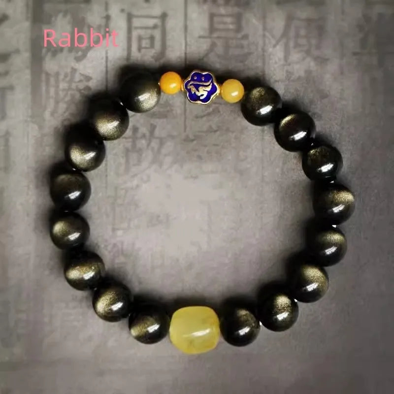 Handmade golden obsidian bracelet with geometric beads and zodiac charm on wrist.