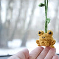 Handmade woven plush frog car pendant in green hanging from rear-view mirror
