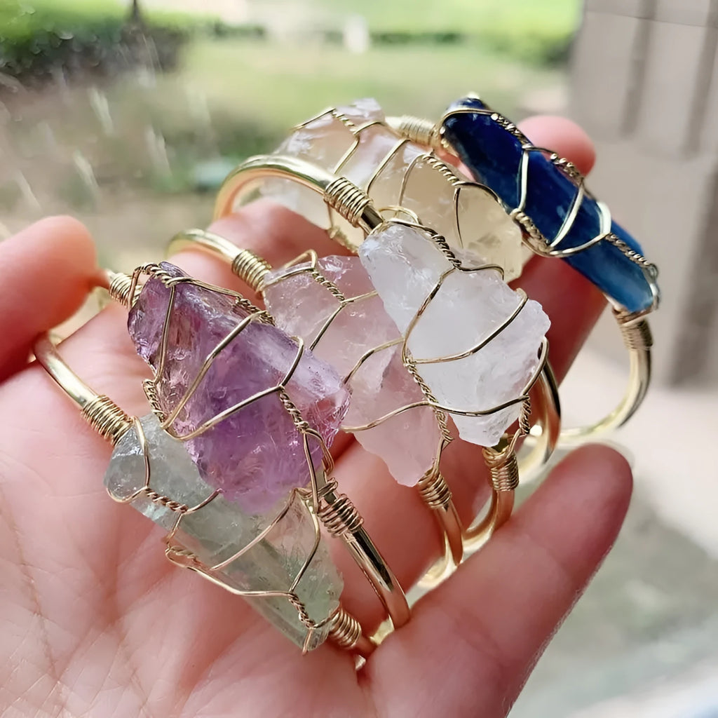 Rough natural crystal bracelet with gold winding geometric design on a wrist.