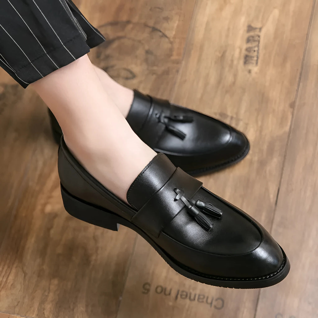 Men's black slip-on business casual shoe with tassel detail and rubber sole.