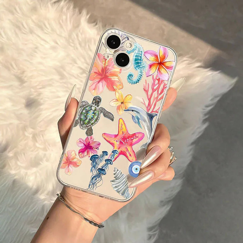 Clear transparent iPhone case with printed blue dolphin, green turtle, shell, and leaf designs.
