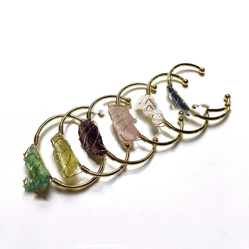 Rough natural crystal bracelet with gold winding geometric design on a wrist.