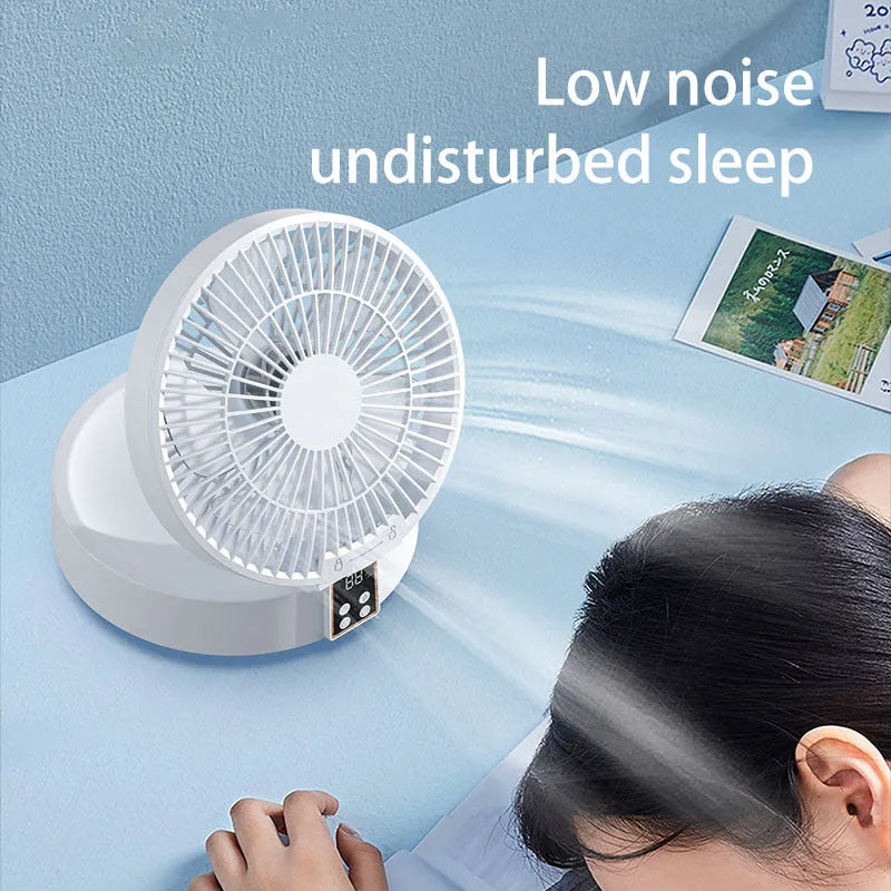 White rechargeable USB ceiling fan with remote control folded on a desk next to its charging cable.