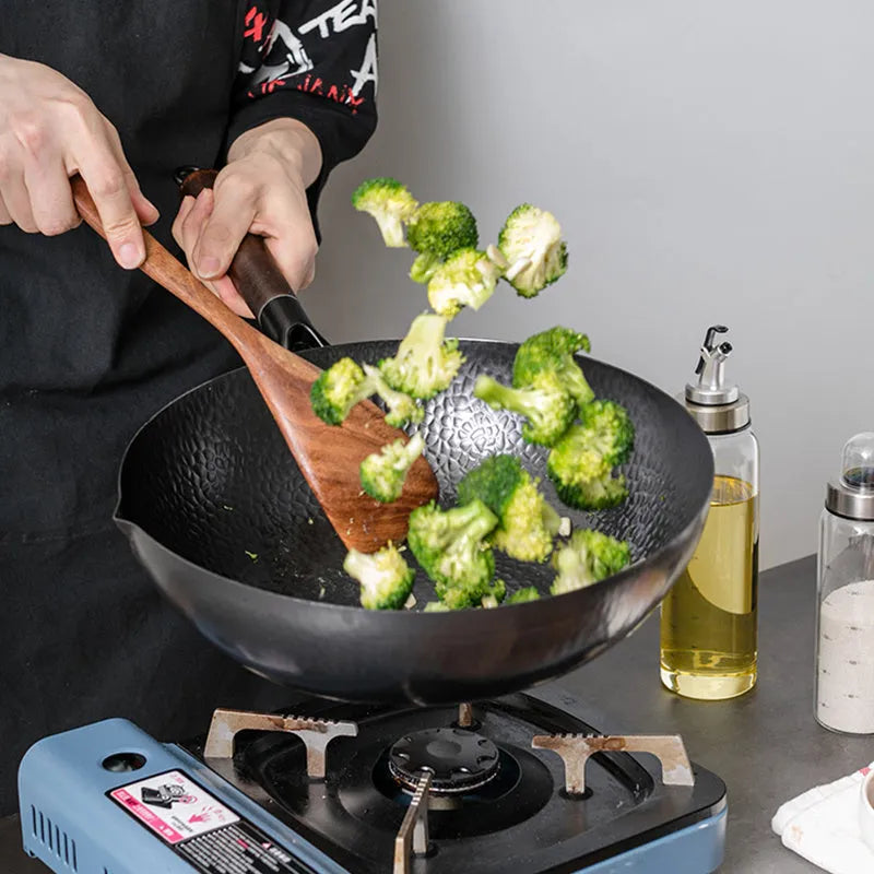 Black traditional iron wok with wooden handle, shown with glass lid.