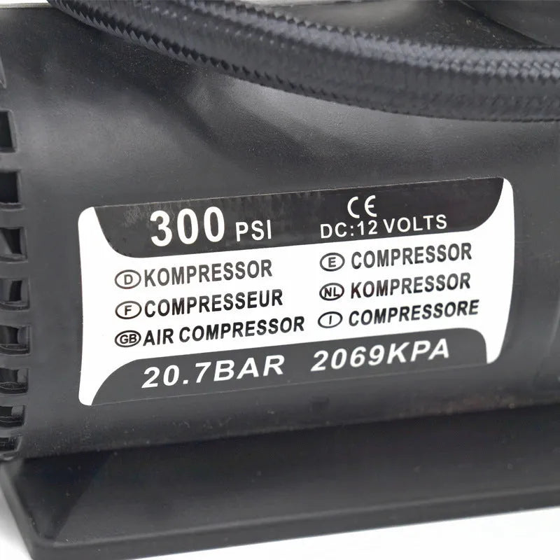 Black portable 12V mini car air compressor with pressure gauge, hose, and two nozzle adapters on grey background