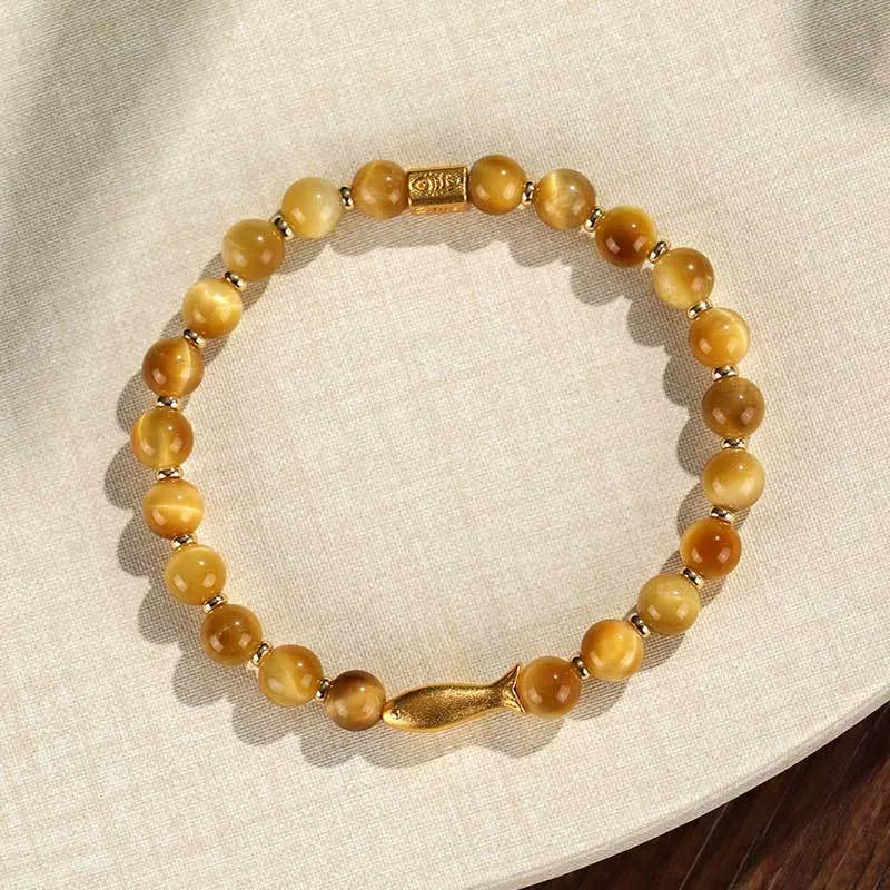 Close-up of a yellow tiger eye beaded bracelet with a detailed small fish charm.
