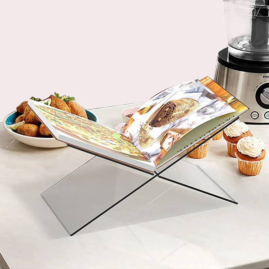 Clear acrylic X-shaped book reading rack displaying a book on a desktop.