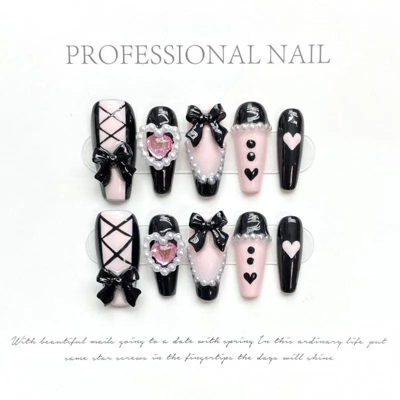 Black and pink heart-shaped hand-painted false nails with bow design, shown in mid-length cat's eye style.