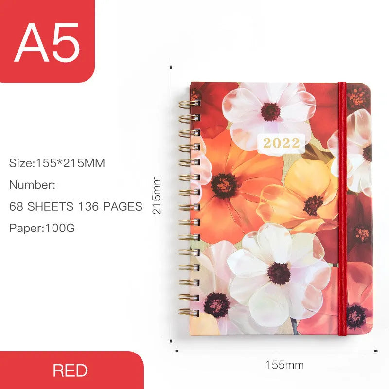 A5 spiral-bound notebook with a colourful floral design cover, lying open on a table.