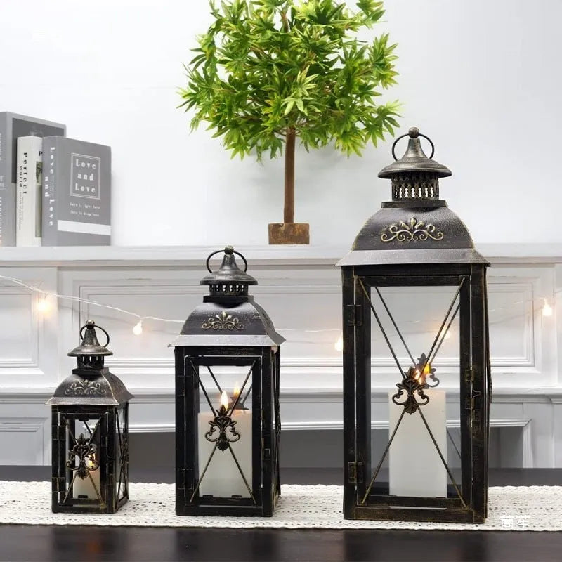 Black and gold wrought iron floor-standing storm lantern with tempered glass panes on a stone patio.