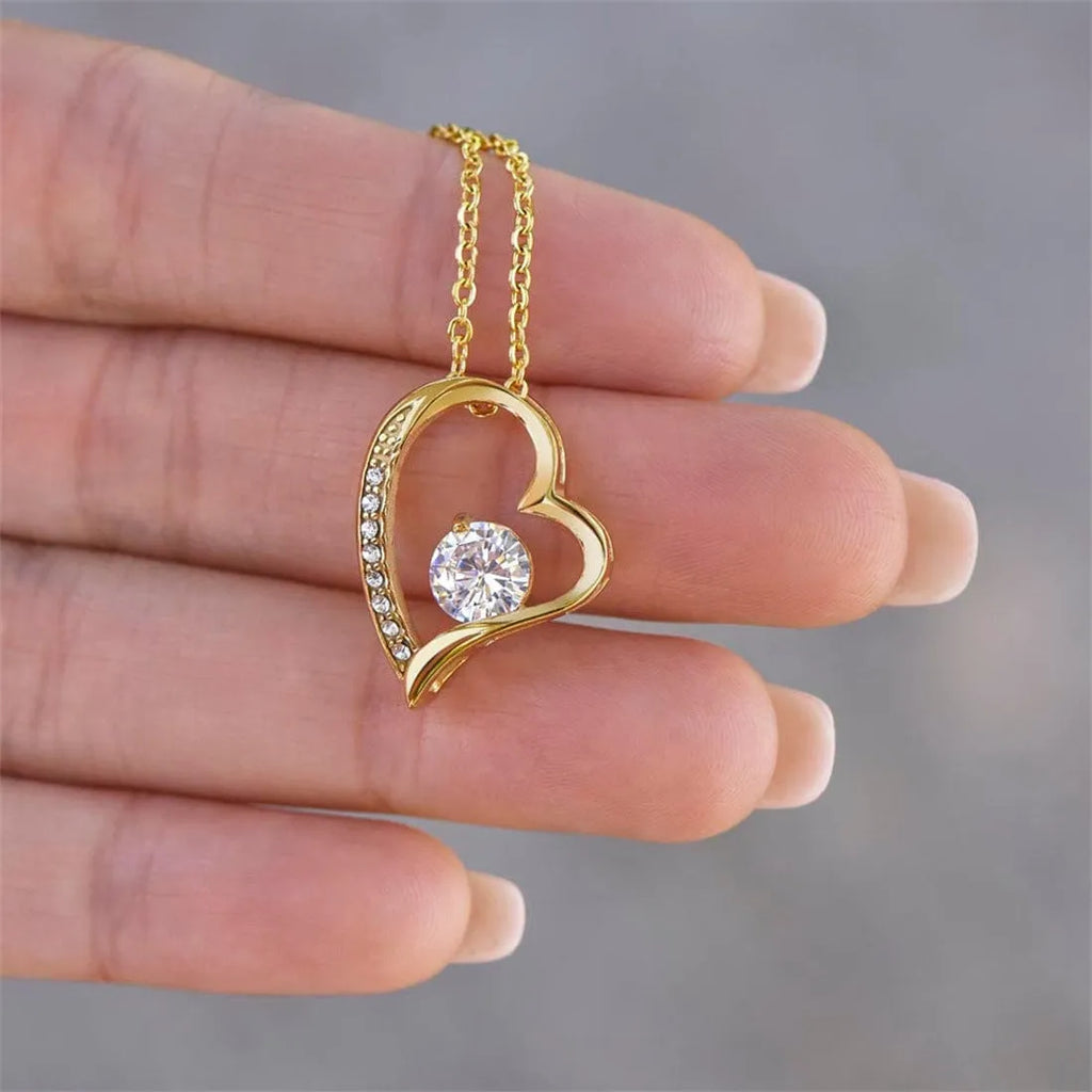 A hollow heart-shaped pendant necklace in a gold or silver finish, presented inside a gift box with a greeting card.