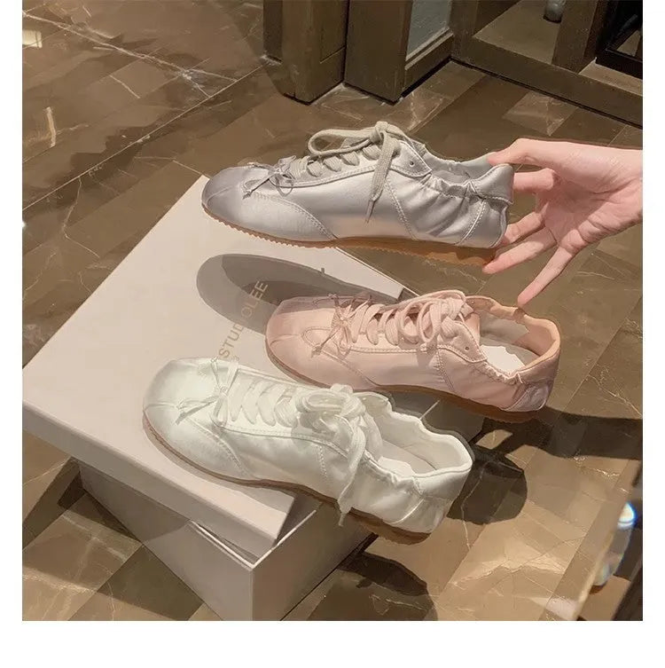 Women's silver satin ballet flats with round toe and white front lace-up on a rubber sole.