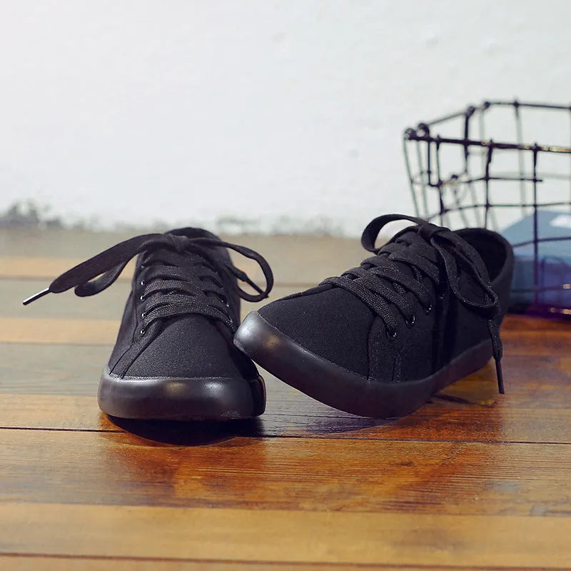All-black women's canvas flat shoes with lace-up front and rubber soles.