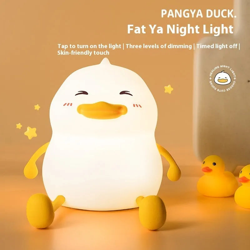 Chubby white silicone night light on a desk holding a mobile phone, showing touch controls and USB port.