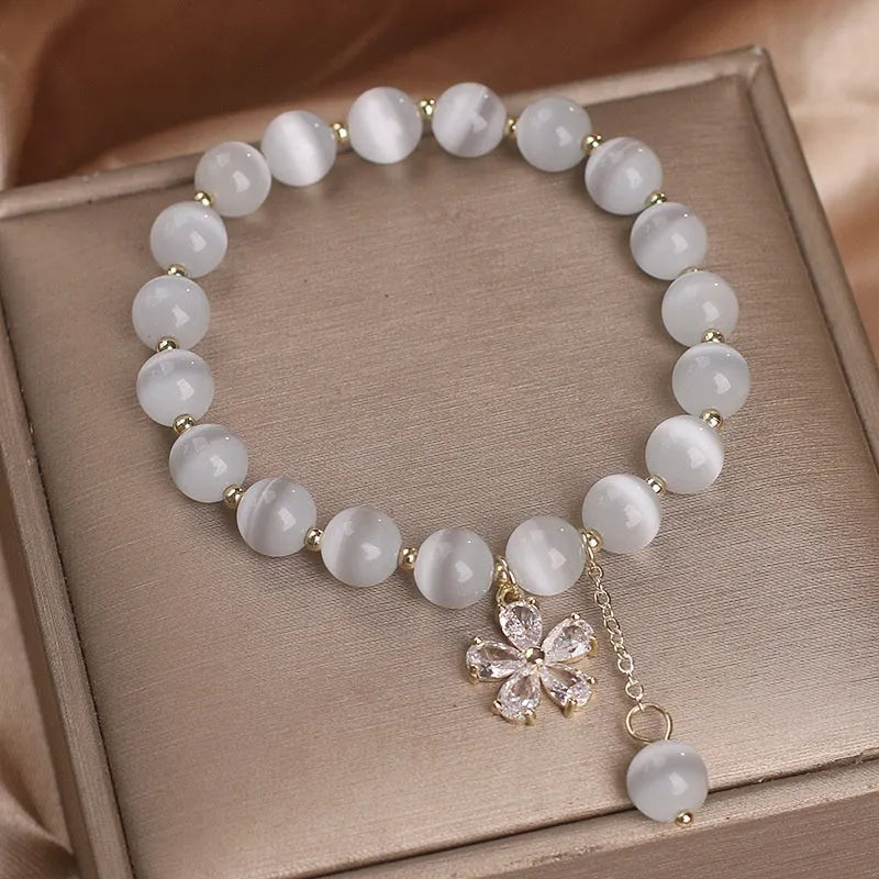 White cat's eye stone single-loop bracelet with a safety buckle, pendant, and small flower tassel decoration.