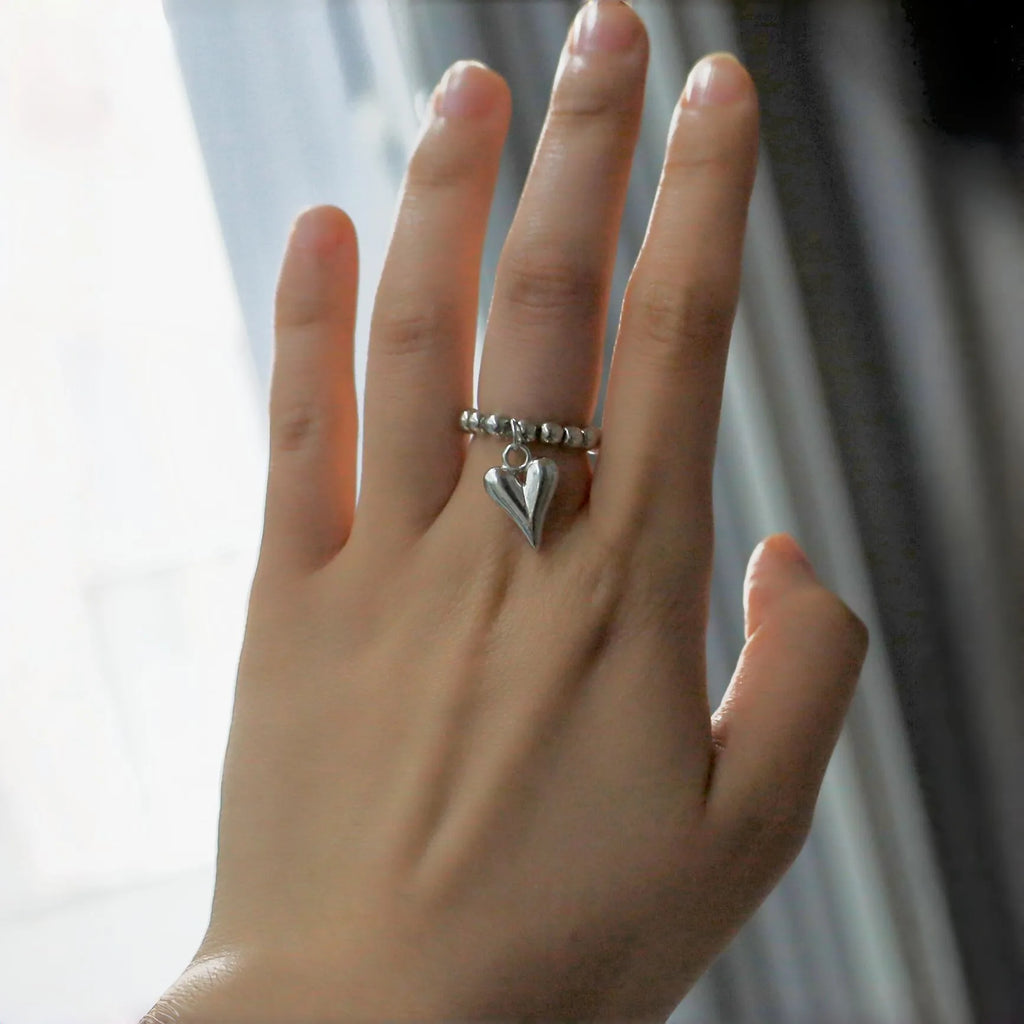 Handmade elastic love ring with geometric beaded string design and heart charm on adjustable band