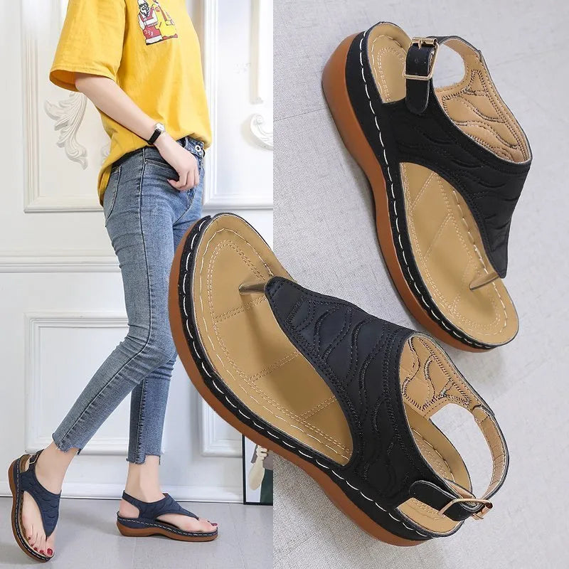 Women's beige wedge heel flip flop sandals with an adjustable buckle strap on a wooden deck.
