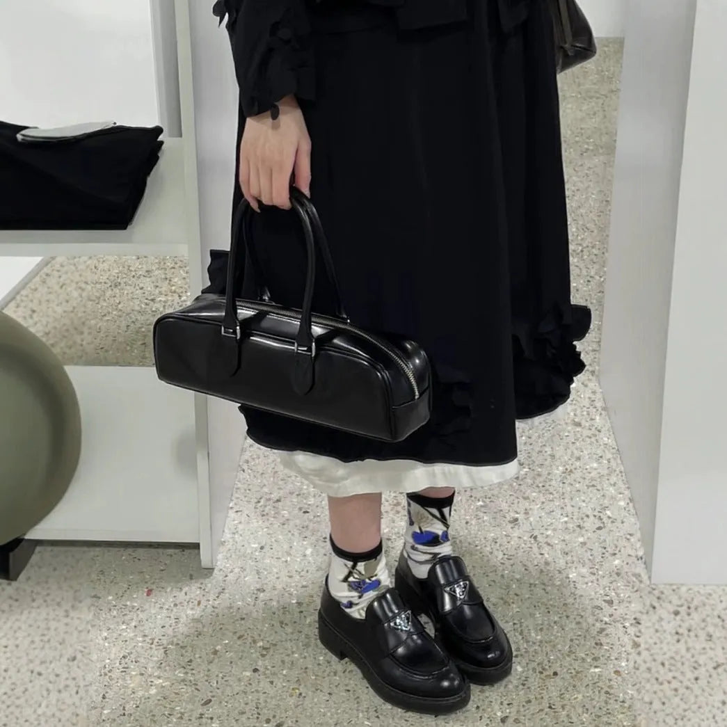 Black corduroy cowhide french stick underarm bag with sewing thread detail on a white background
